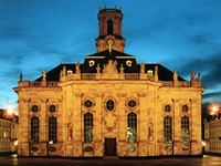 Das Foto basiert auf dem Bild "Ludwigskirche bei Nacht Haupteingang" aus dem zentralen Medienarchiv Wikimedia Commons ist unter der GNU-Lizenz für freie Dokumentation. Der Urheber des Bildes Alexander Spät.